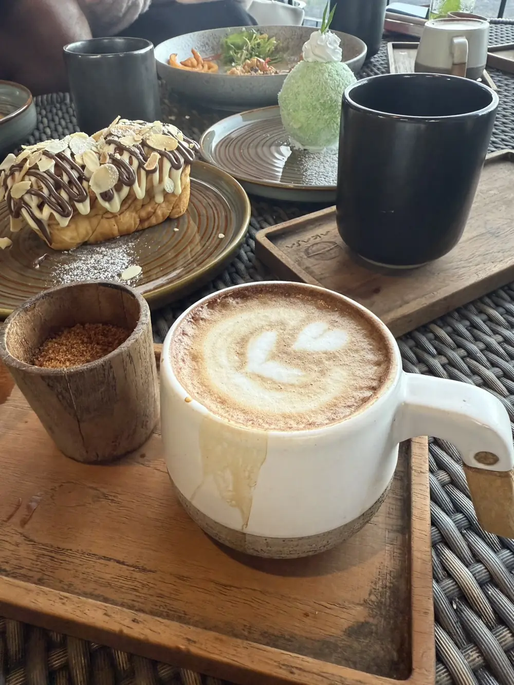 A latte with latte art next to a slice of cake on a wooden tray at Akasa Specialty Coffee, Kintamani, Bali