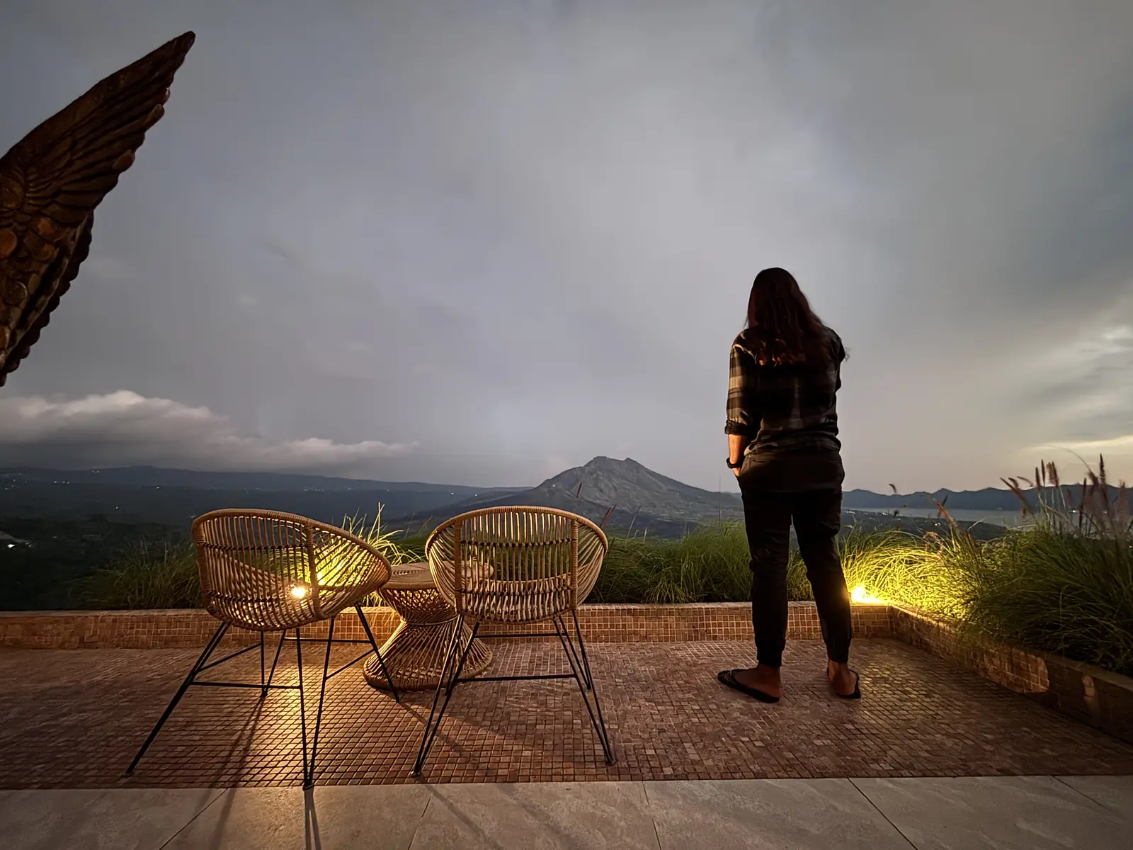 A visitor on the open-air terrace at Akasa Specialty Coffee at dawn, looking out over Mount Batur and the caldera lake in Kintamani, Bali