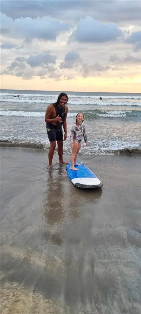 Andrew with a young student standing on a soft surfboard at Kuta Beach, Bali