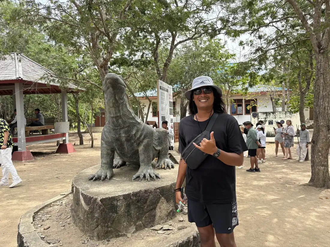 Andrew standing beside the Komodo dragon statue at the ranger station on Komodo Island, with visitors and trees in the background