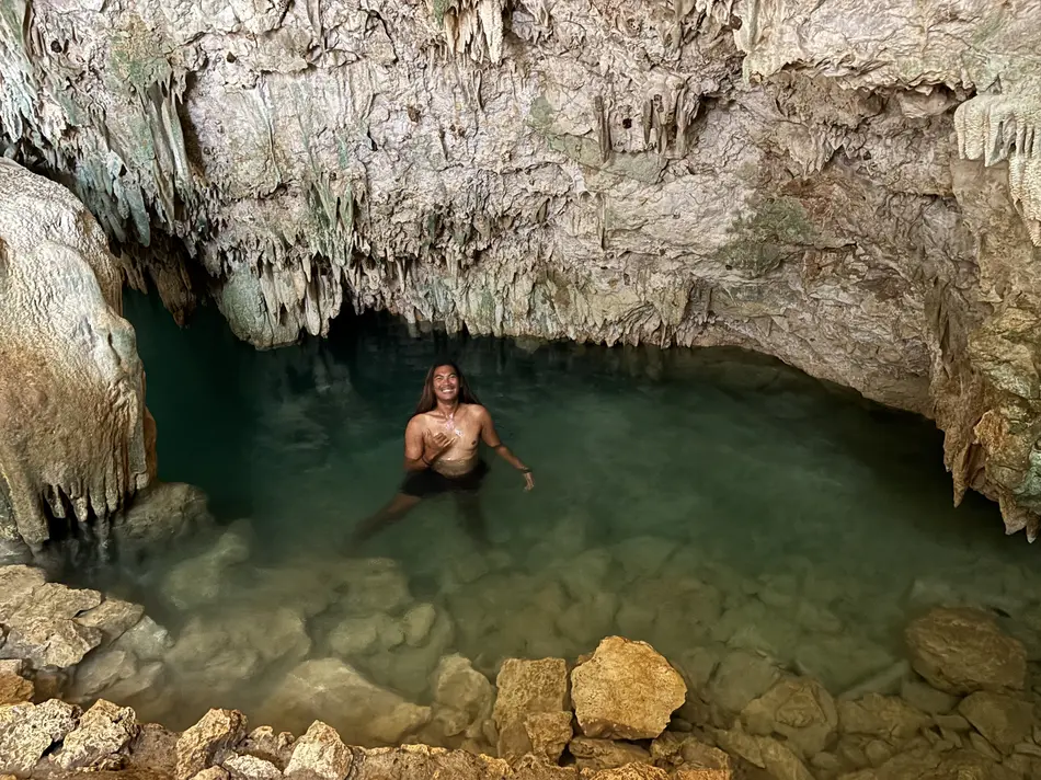 A visitor swimming in the natural saltwater pool inside Rangko Cave near Labuan Bajo, lit by an opening in the limestone ceiling above