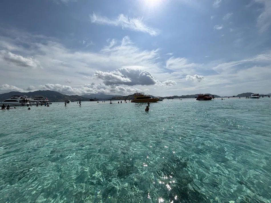 The clear turquoise water and white sandbar at Taka Makassar in Komodo National Park, with boats and swimmers in the distance