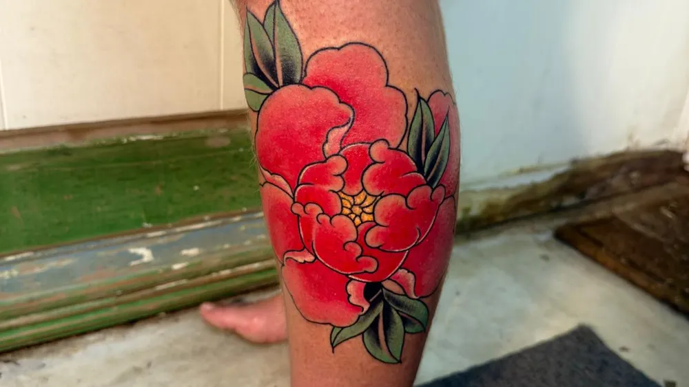 Bold Japanese peony tattoo on the calf, deep red and green, done at a licensed Kuta Bali studio