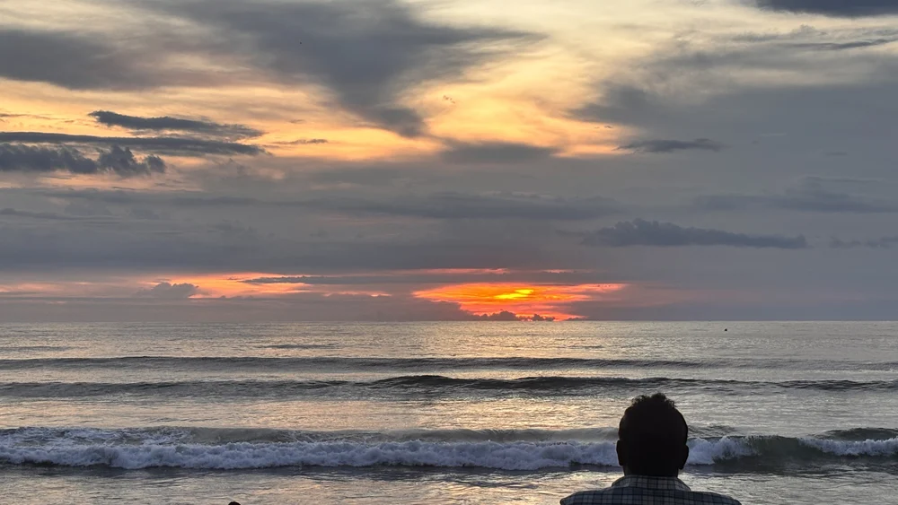 People sitting on plastic chairs on Kuta Beach watching the sun set under a heavy cloudy sky, Bali