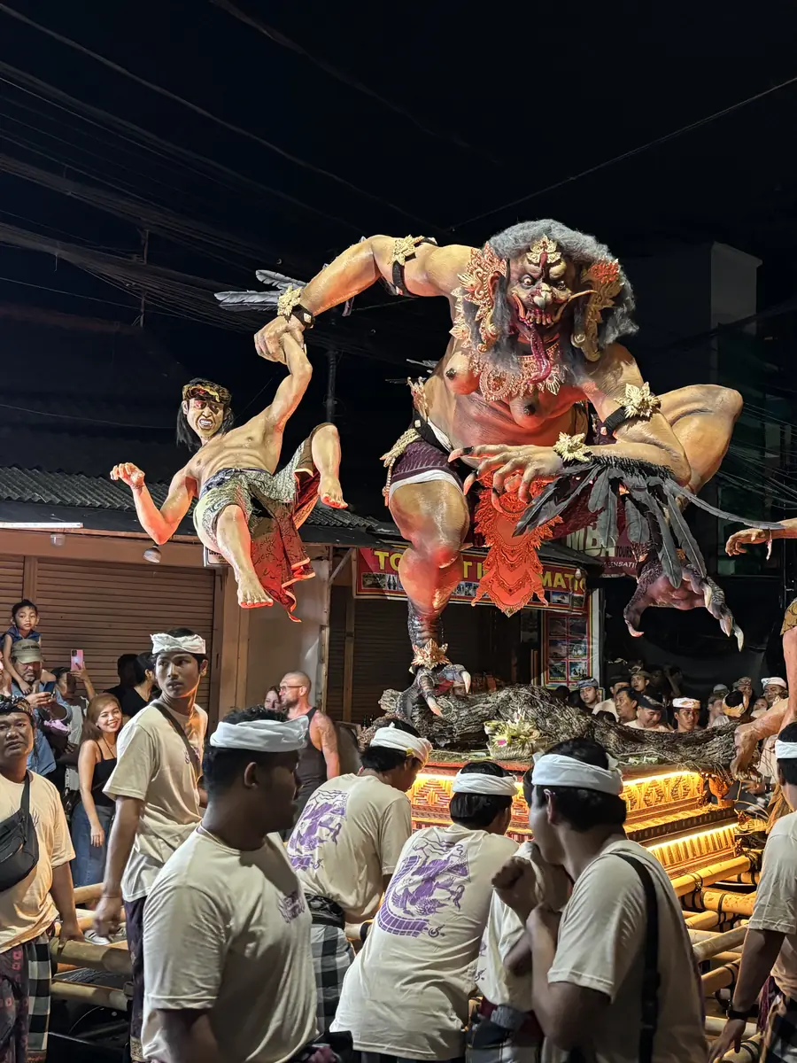 A red demon Ogoh-Ogoh effigy hoisted above the carrier team on a Kuta street at night during the Nyepi eve parade, Bali