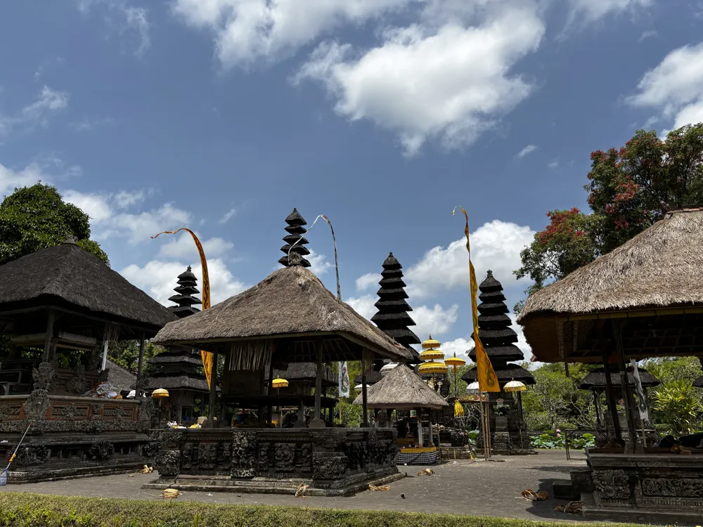 The tiered meru towers and thatched pavilions of Taman Ayun temple in Mengwi, Bali, with penjor poles and ceremonial umbrellas in the courtyard