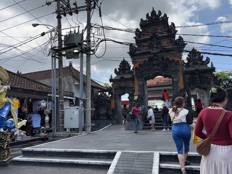 The main entrance gate at Tanah Lot with souvenir stalls on both sides and visitors walking up the steps towards it, Bali