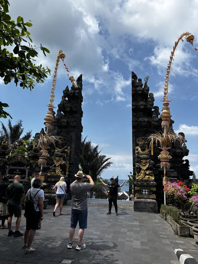 The split candi bentar gate at the entrance to Tanah Lot temple, with penjor bamboo poles, gold guardian figures and the Pura Luhur Tanah Lot stone sign, Bali