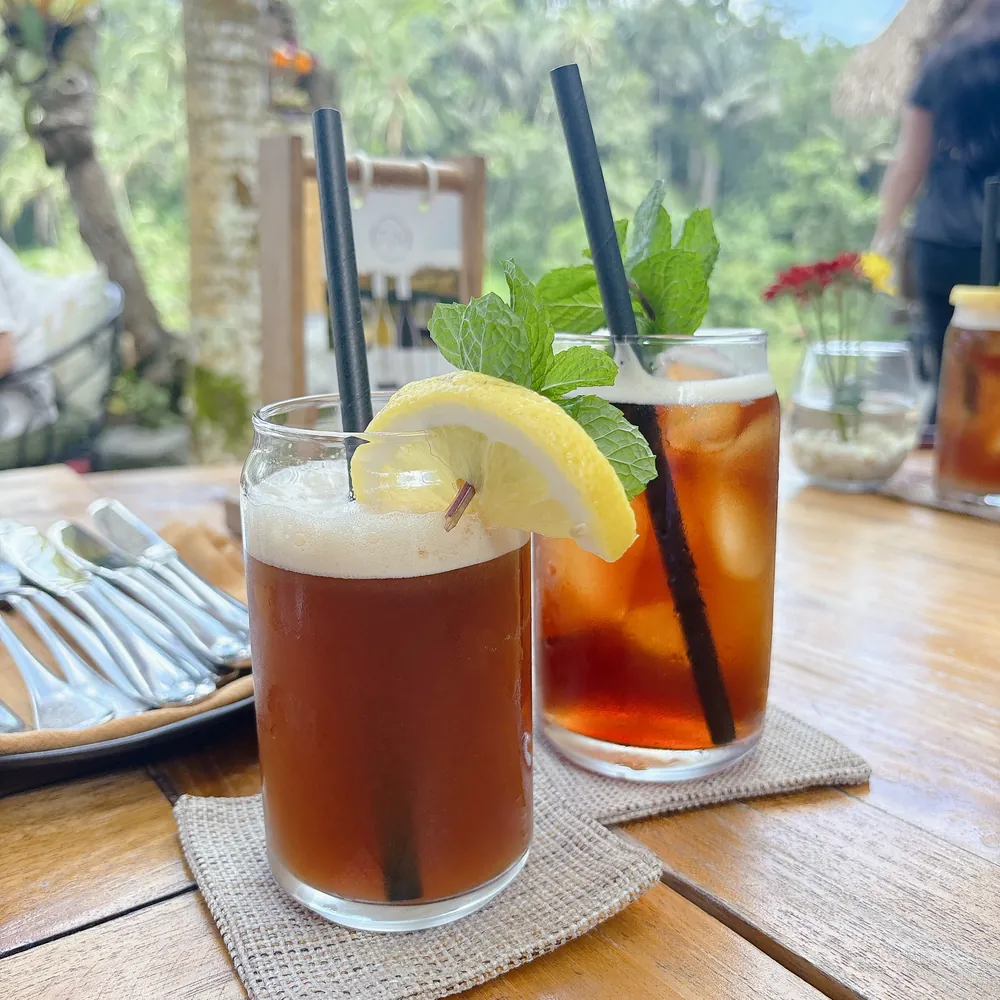 Two iced drinks with lemon on a wooden table at TIS Cafe with the jungle behind, near Ubud, Bali