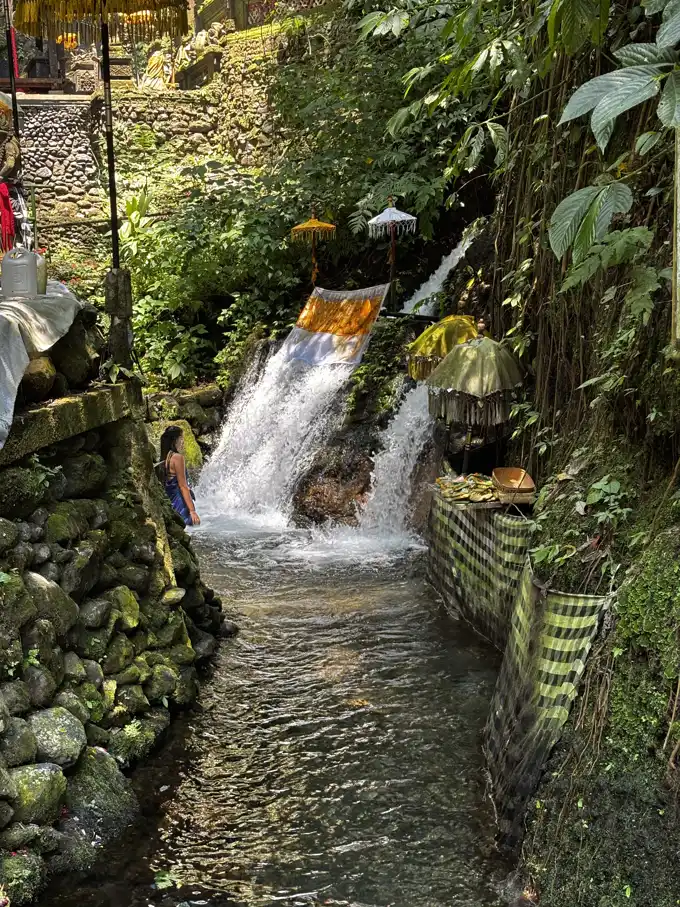 A line of stone spouts pouring cold spring water into a bathing pool at an Ubud spring temple