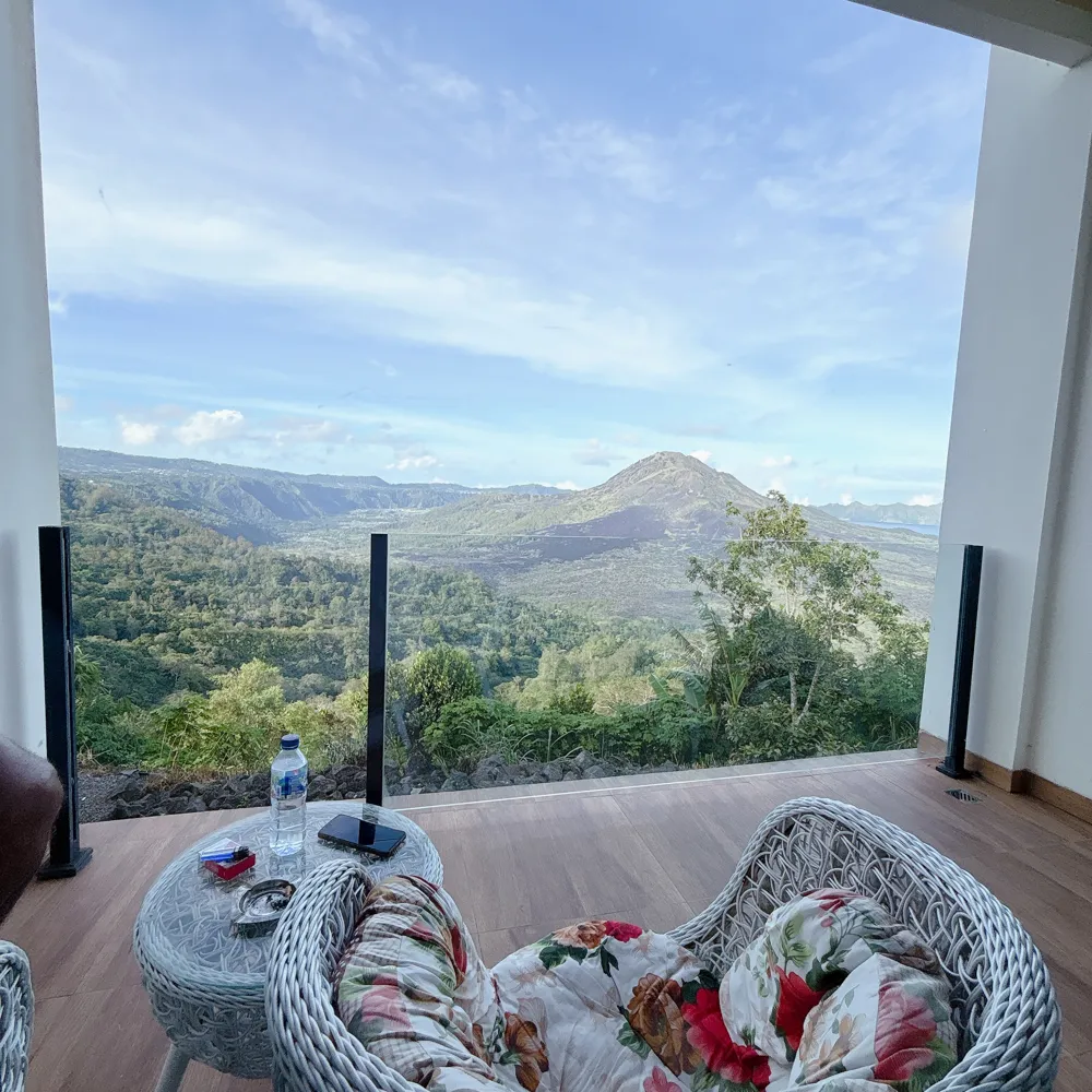 A guesthouse balcony with rattan chairs looking out over the Kintamani caldera and Mount Batur, Bali