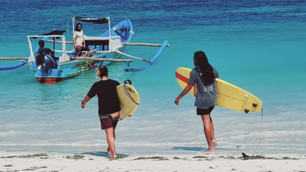 Turquoise water, a traditional jukung boat and surfers walking a white-sand Bali beach with island headlands