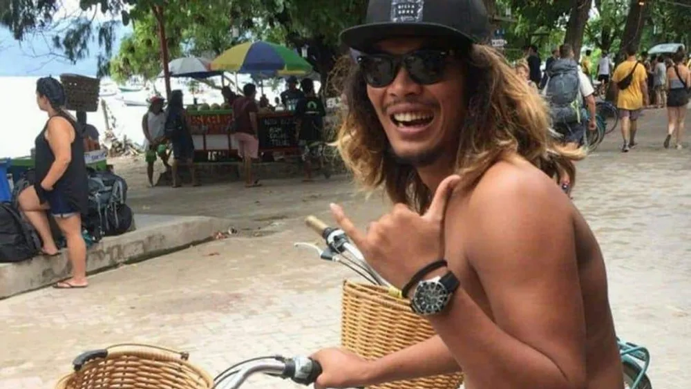 Andrew, a local Bali guide, smiling with a shaka sign on his bicycle on a Kuta street